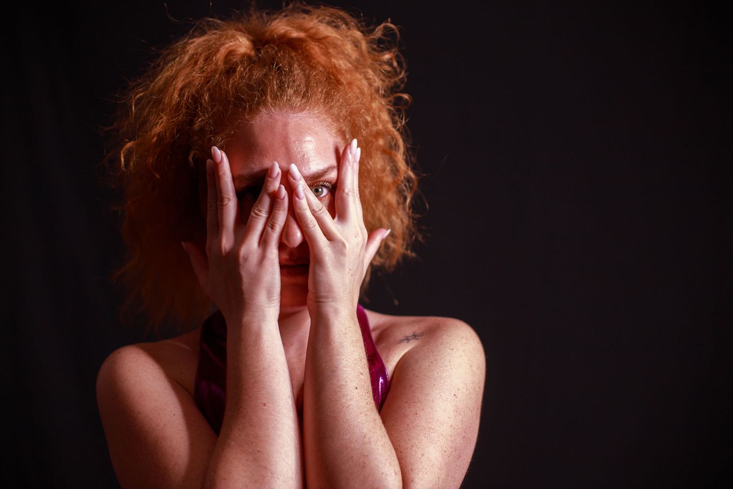 Emotional portrait series with hands covering face against dark backdrop.