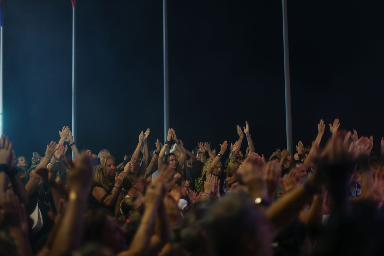 Concert crowd with raised hands silhouetted against dark stage lights.