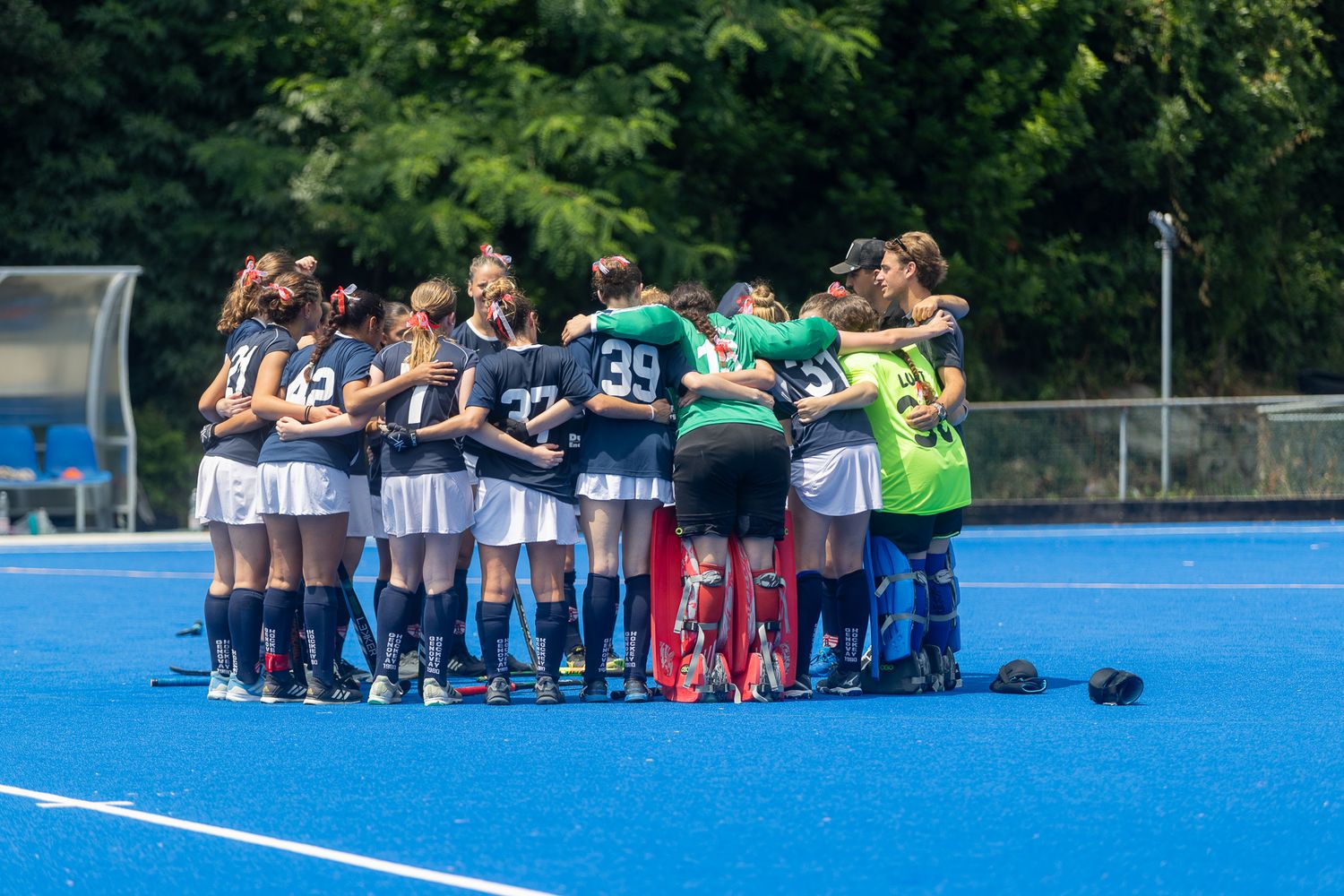 Sports teams huddle together on a blue hockey field for team meetings.