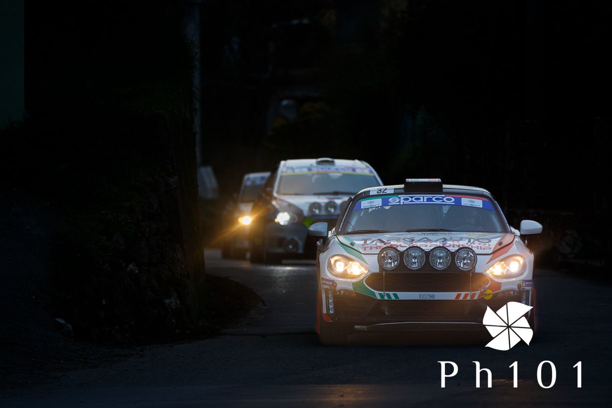 Rally cars with bright headlights racing through a dark forest course.