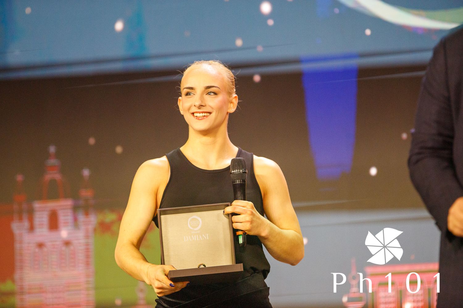 Award recipient holding a plaque on stage at an awards ceremony.