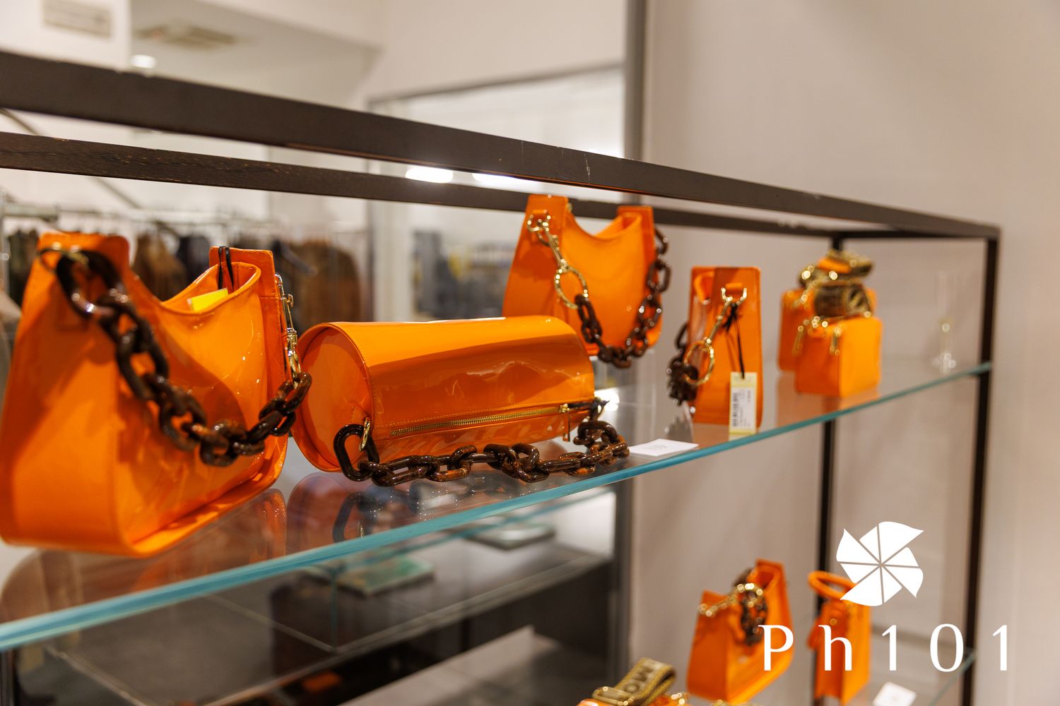 Display of bright orange designer handbags arranged on glass shelves in luxury retail setting.