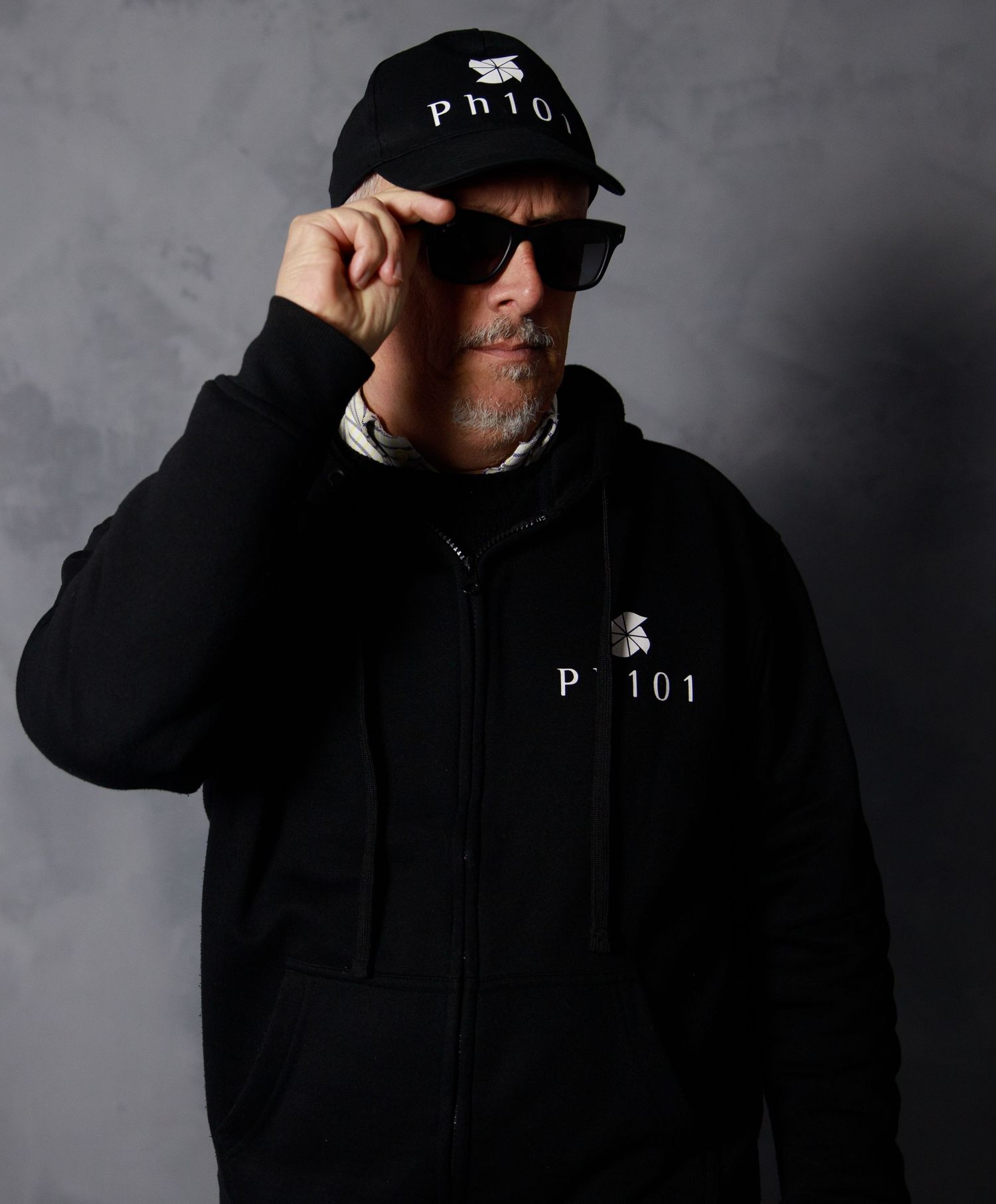 Moody portrait of figure in black hoodie with Ph101 text on cap against gray background.