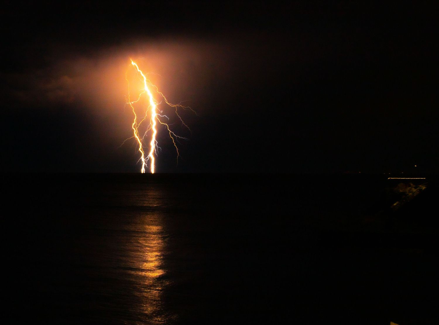 Series of lightning strikes illuminating the dark night sky over water.