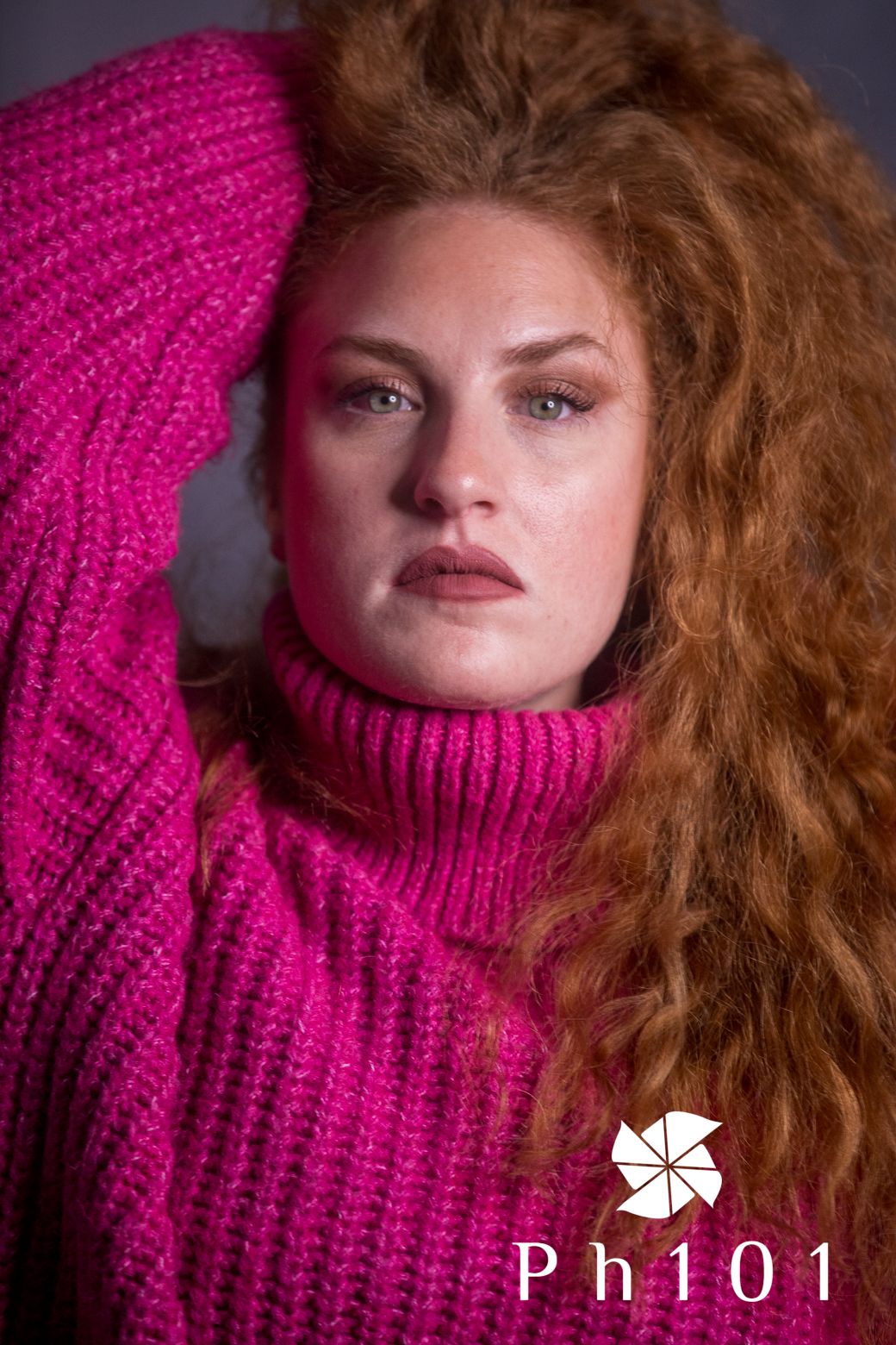 Dramatic portrait with bright pink turtleneck sweater and flowing curly hair.
