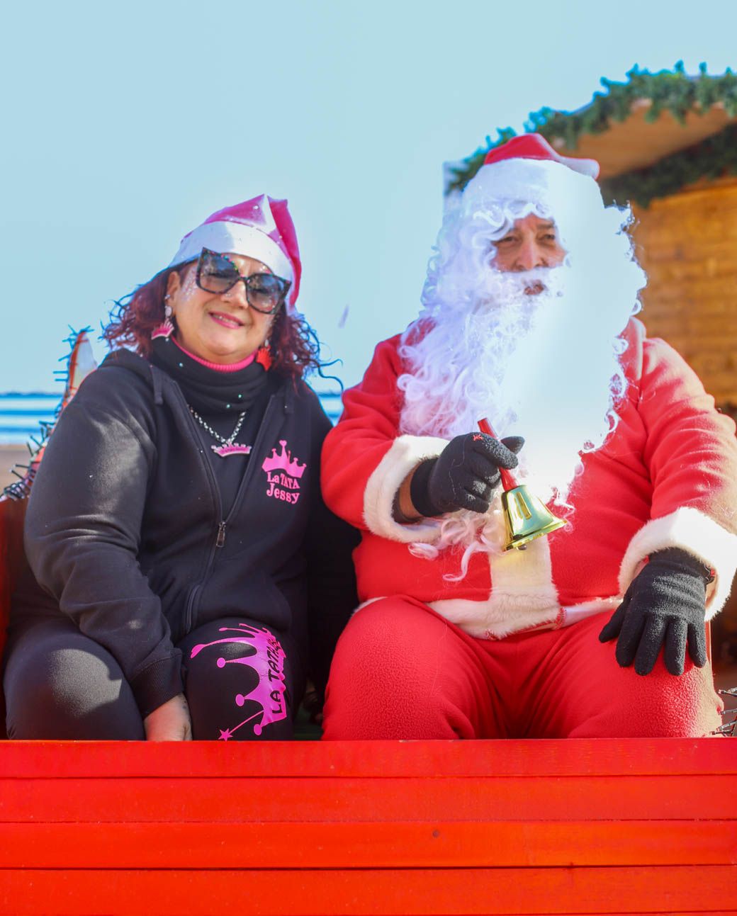 Holiday characters seated on a bright red sleigh against a sunny blue sky backdrop.