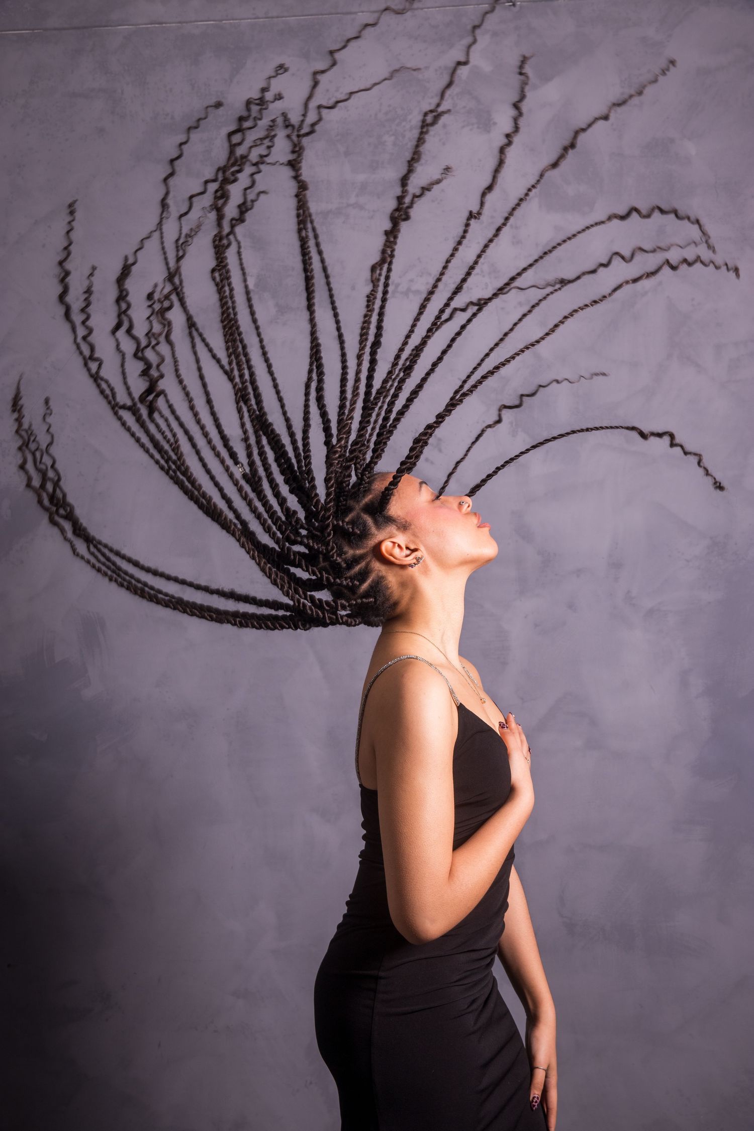 Dynamic motion shot showing long braids swinging through the air against a gray background.