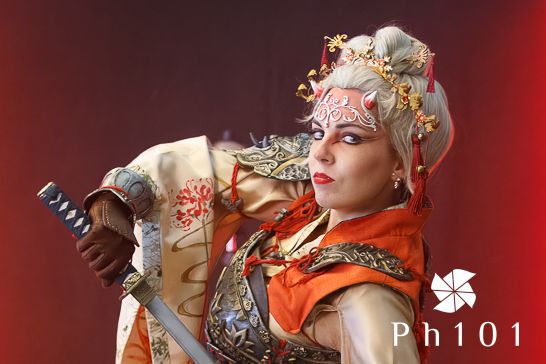 Performers in elaborate gold and red costumes pose dramatically against a dark background.