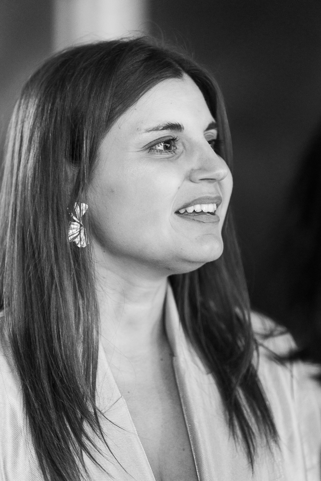 Black and white portrait of a smiling young woman with long dark hair wearing elegant earrings and a light blazer.