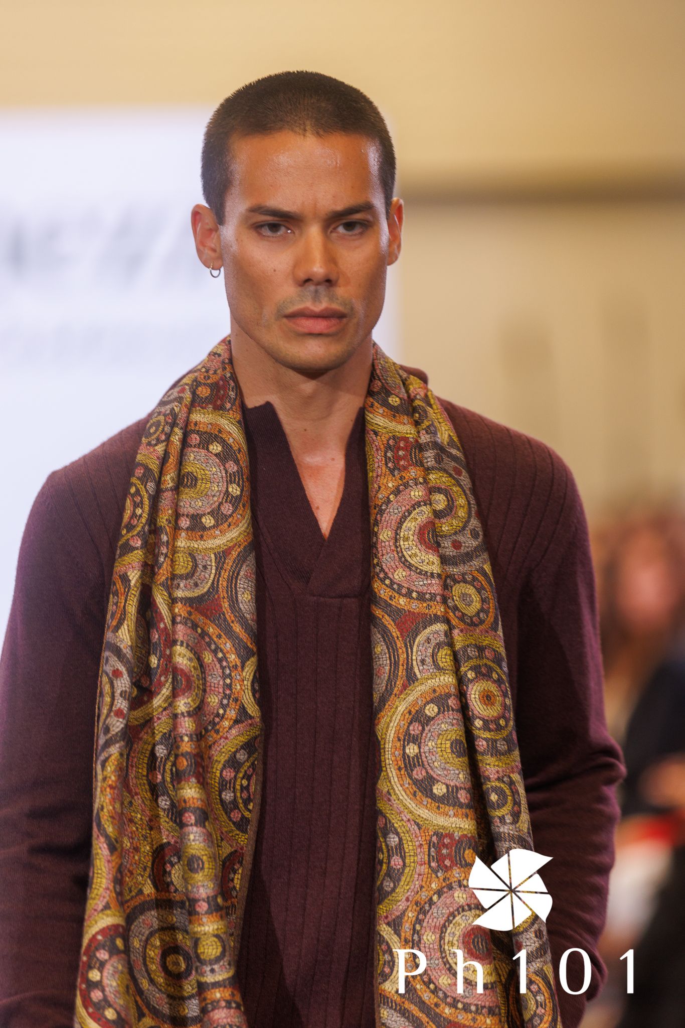 Runway model wearing burgundy top with paisley-patterned scarf at fashion show.