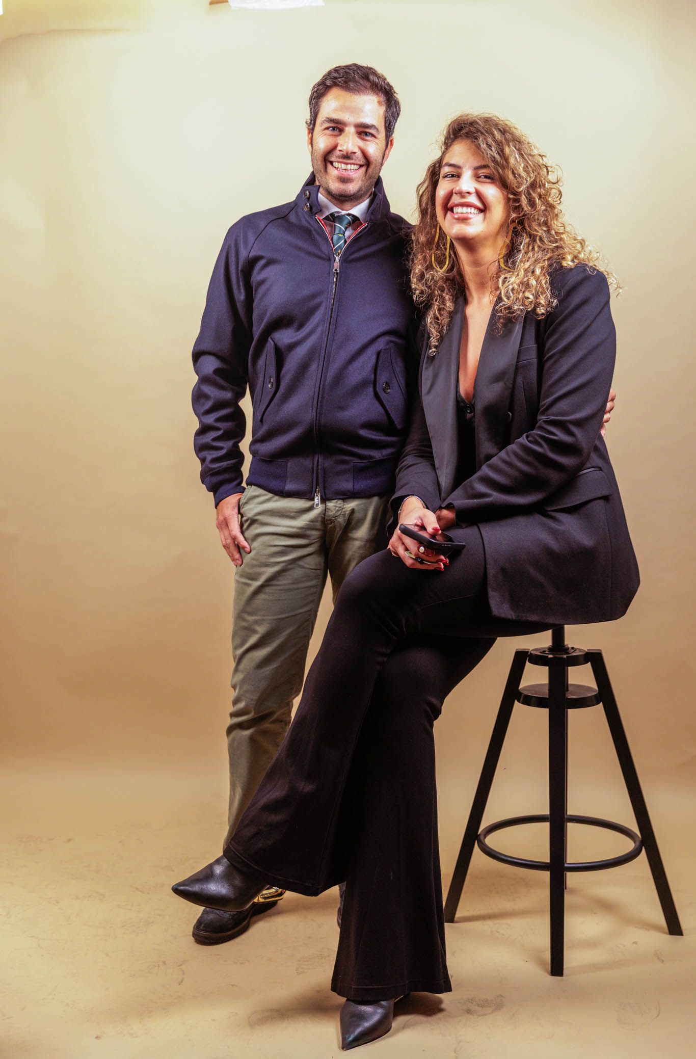 Professional studio portrait of couple in business attire against beige backdrop.