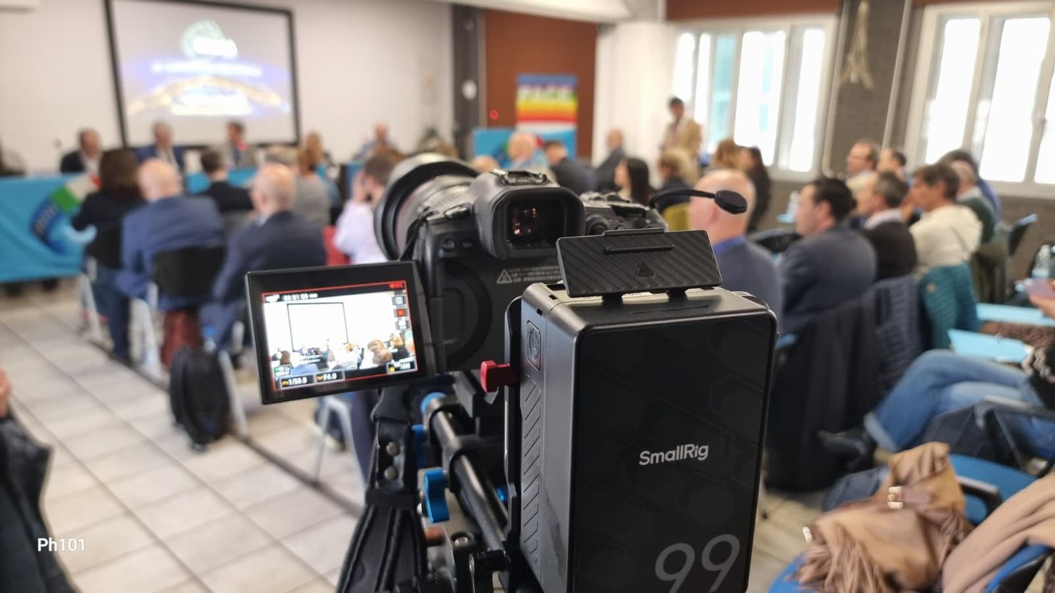 A SmallRig camera on a tripod recording a conference room full of attendees during a professional seminar event.