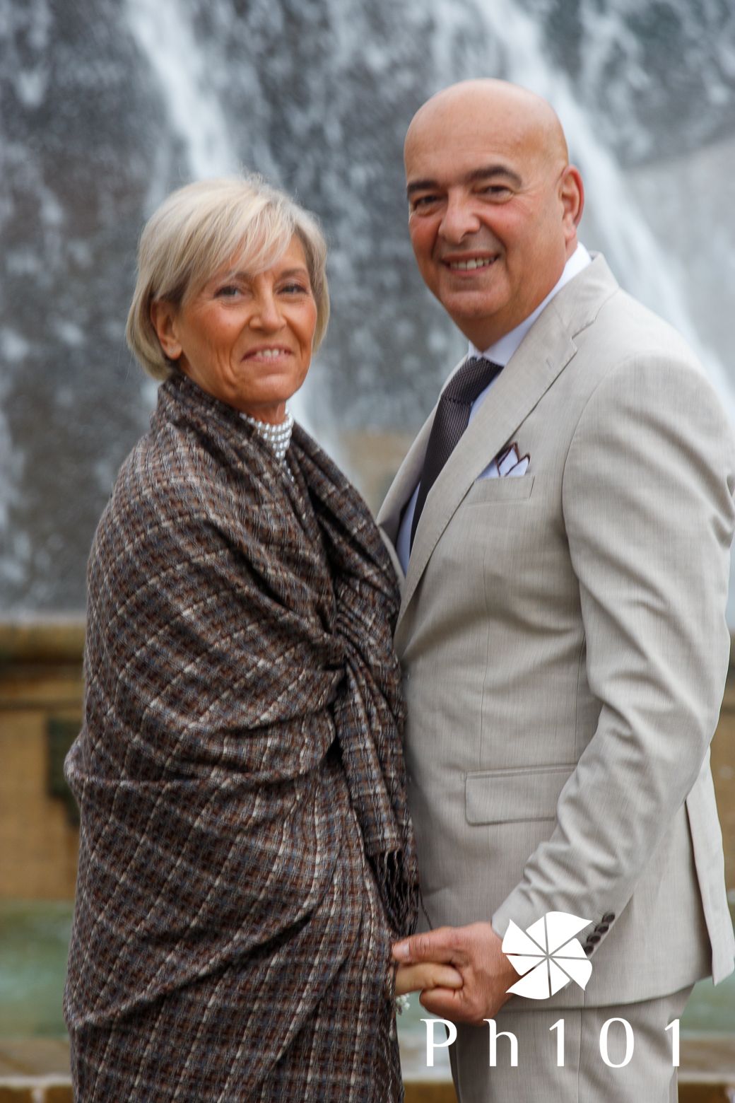 Couple in formal attire smiling together in front of a waterfall backdrop.
