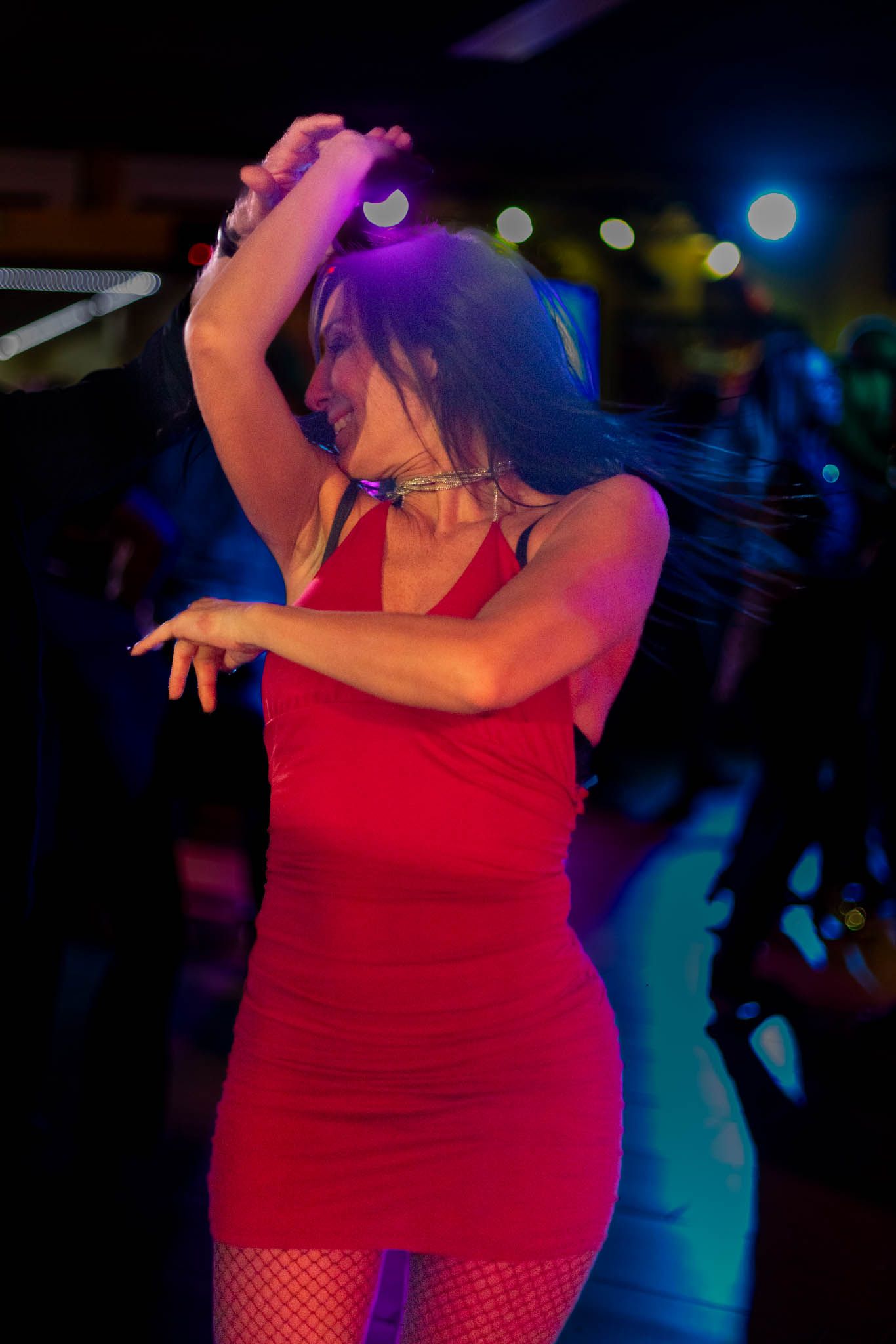 A dancer in a red dress moves energetically under colorful nightclub lighting.