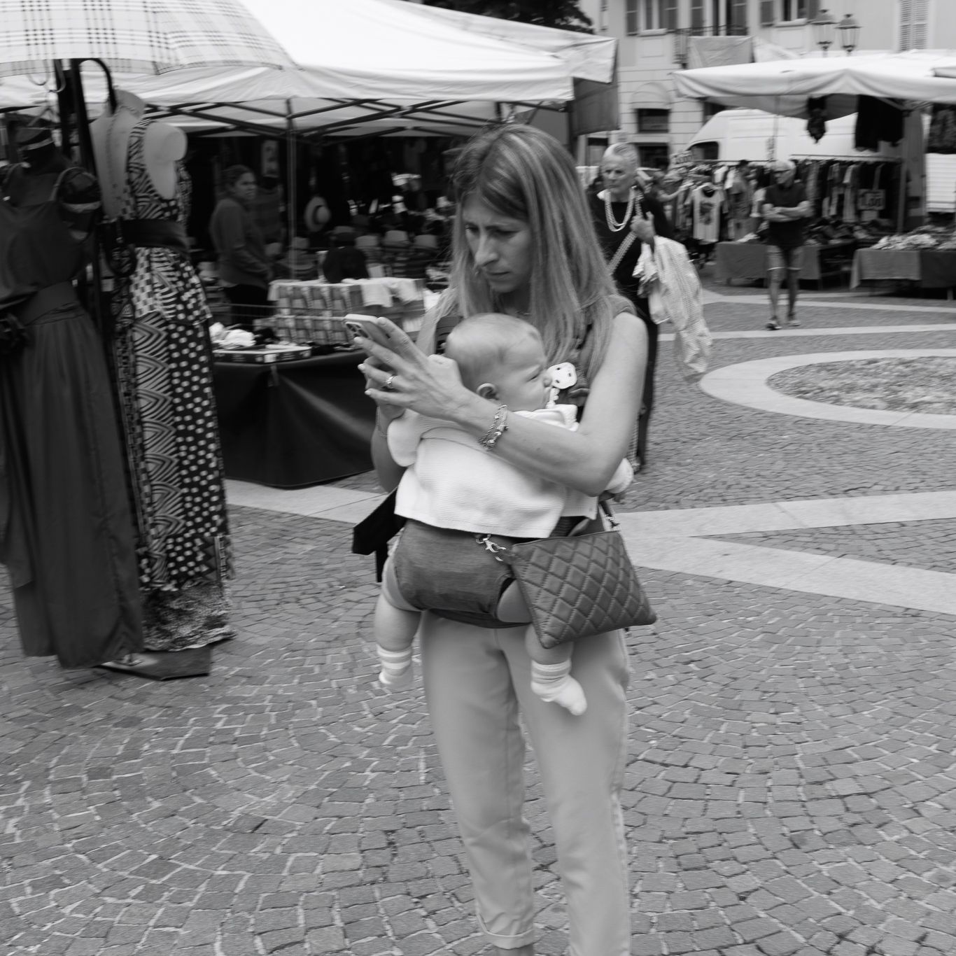 Black and white street photo of person checking phone in outdoor market setting.