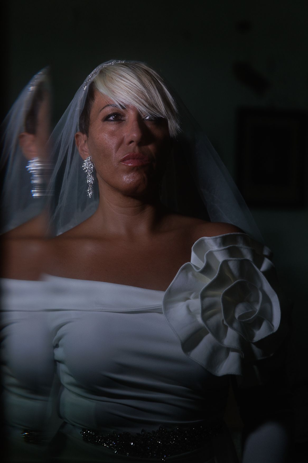 Dramatic bridal portrait featuring an off-shoulder white gown with ruffle detail and flowing veil.