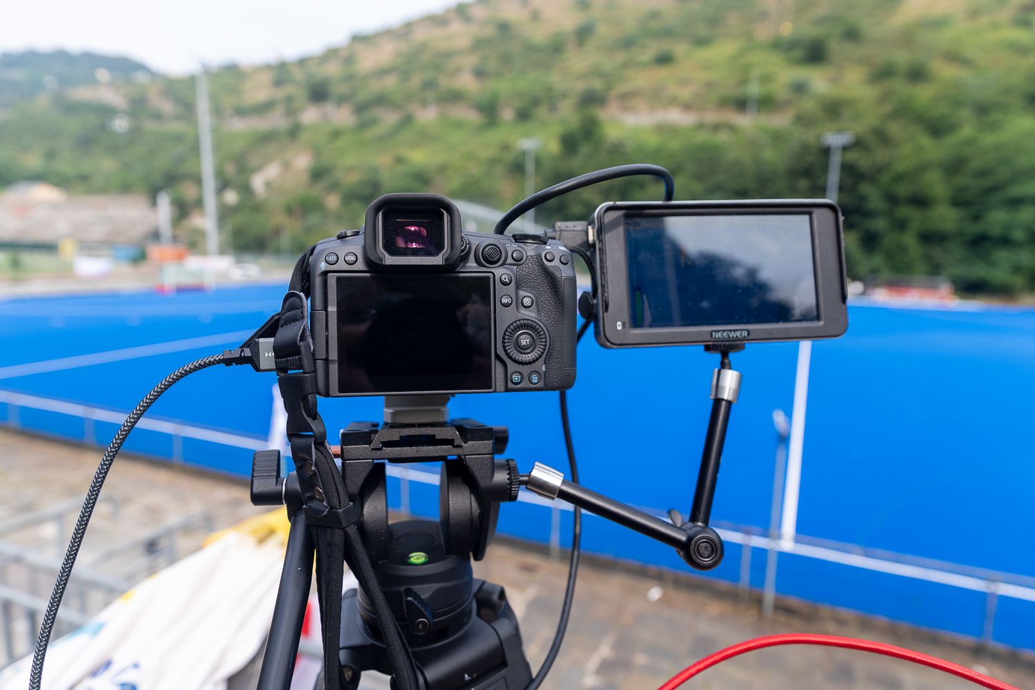Professional camera equipment mounted on tripods overlooking a blue sports field.