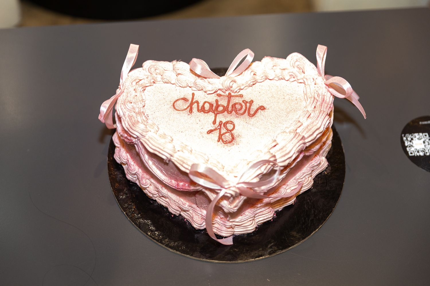 A series of pink frosted cupcakes arranged in a row on a dark surface shows varying levels of frosting detail.