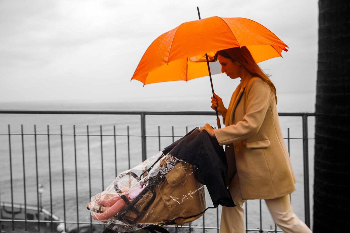 Row of people holding orange umbrellas against grey sky backdrop.