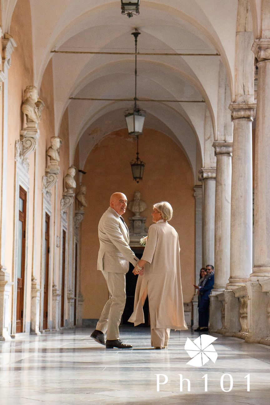 Couple in light colored clothing holding hands in a beautiful classical colonnade with arched ceilings.