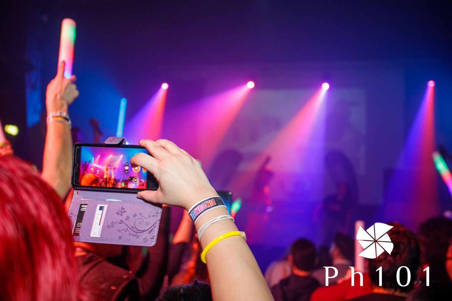 Hand holding phone recording concert with colorful stage lights in background.