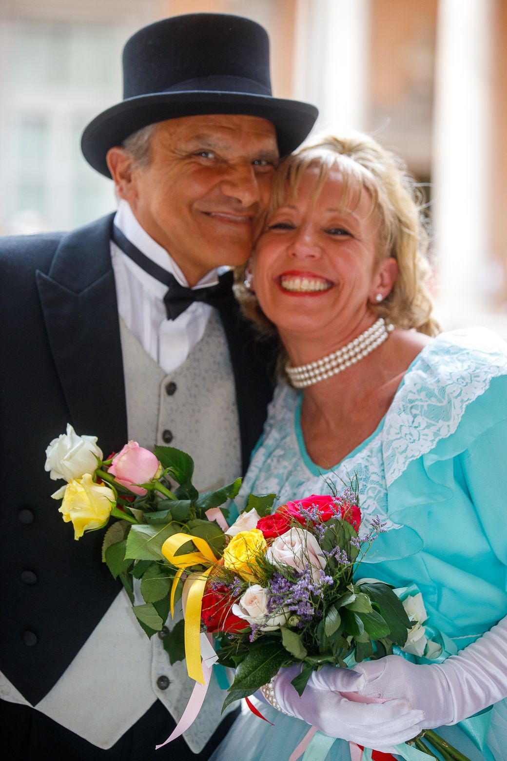 Couple in formal attire holding bouquet with yellow roses and ribbons.