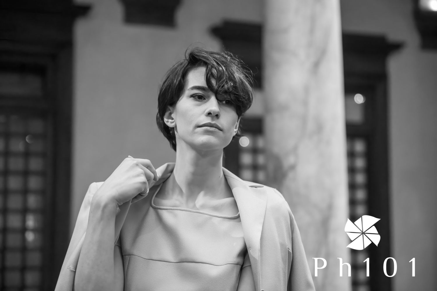 Person in a light colored outfit poses against a wall with columns in black and white photography.