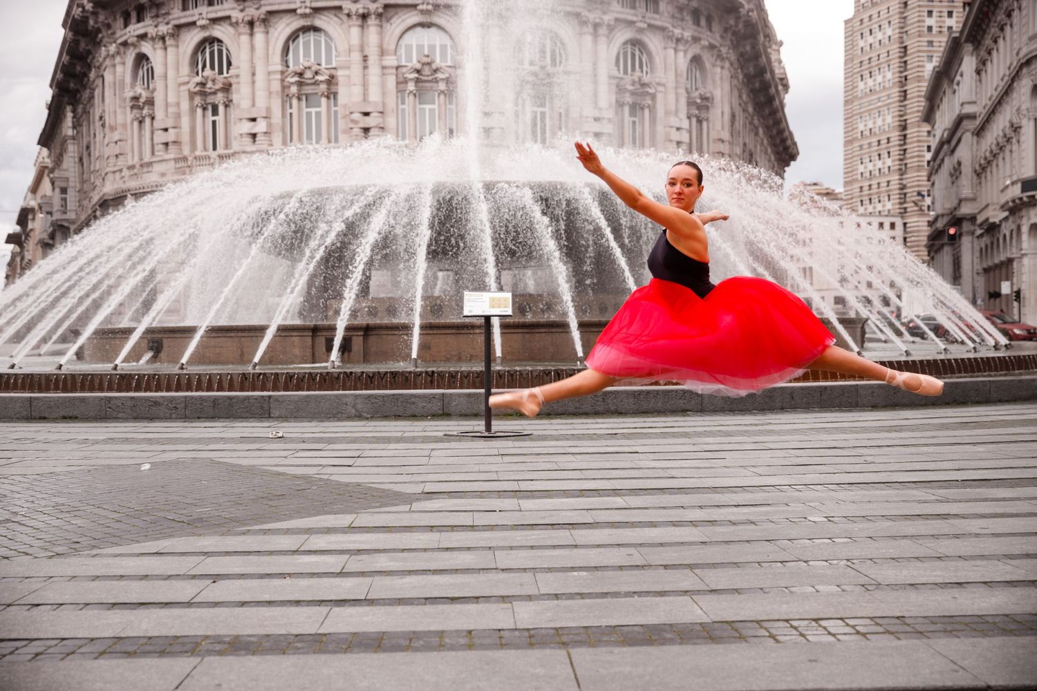 Ballet dancer in red dress performing graceful movements on stone steps near ornate architecture.