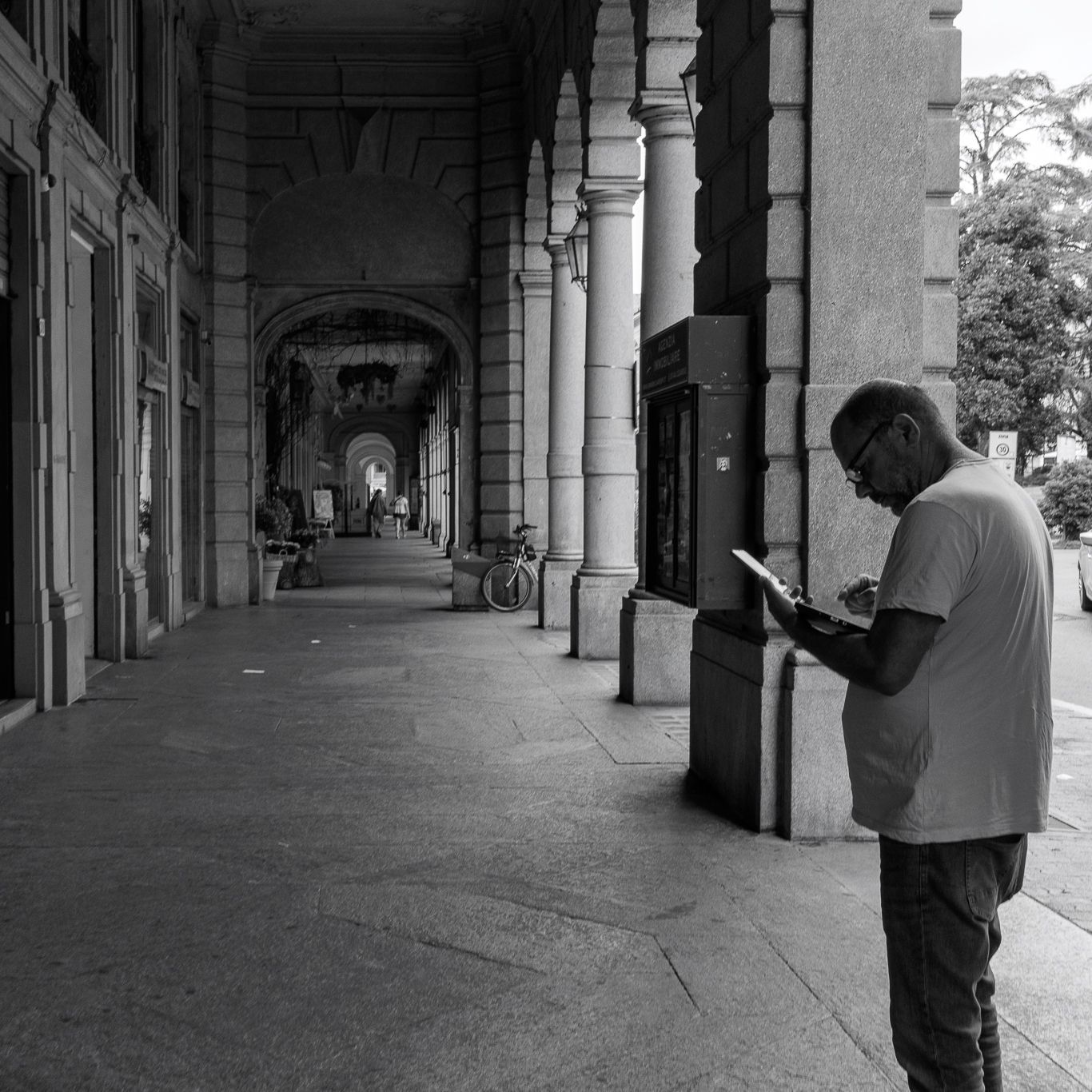 Person reading phone under covered walkway with classical columns.