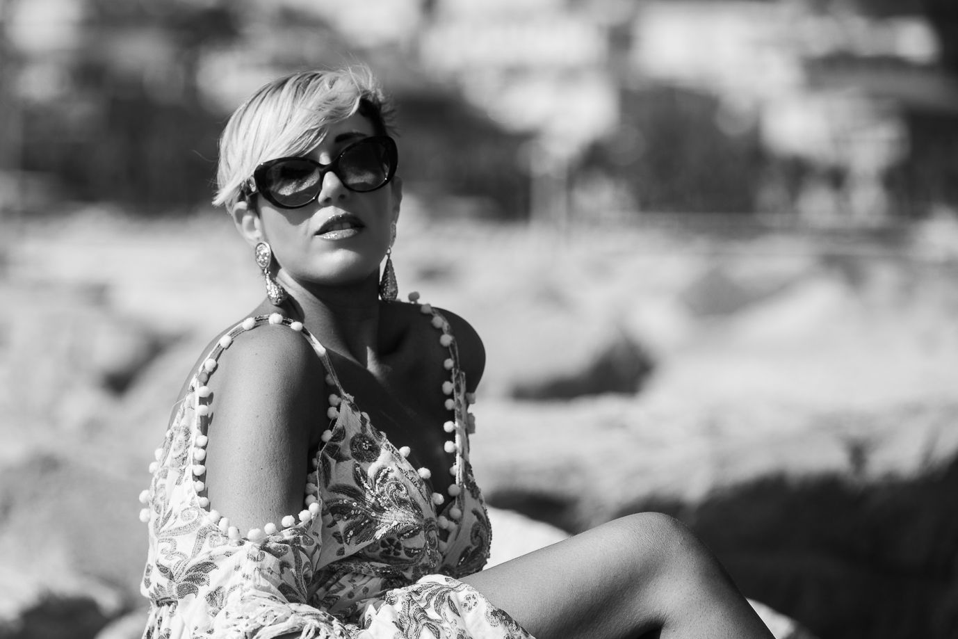 Woman in sunglasses and summer attire poses in black and white vintage style photography.