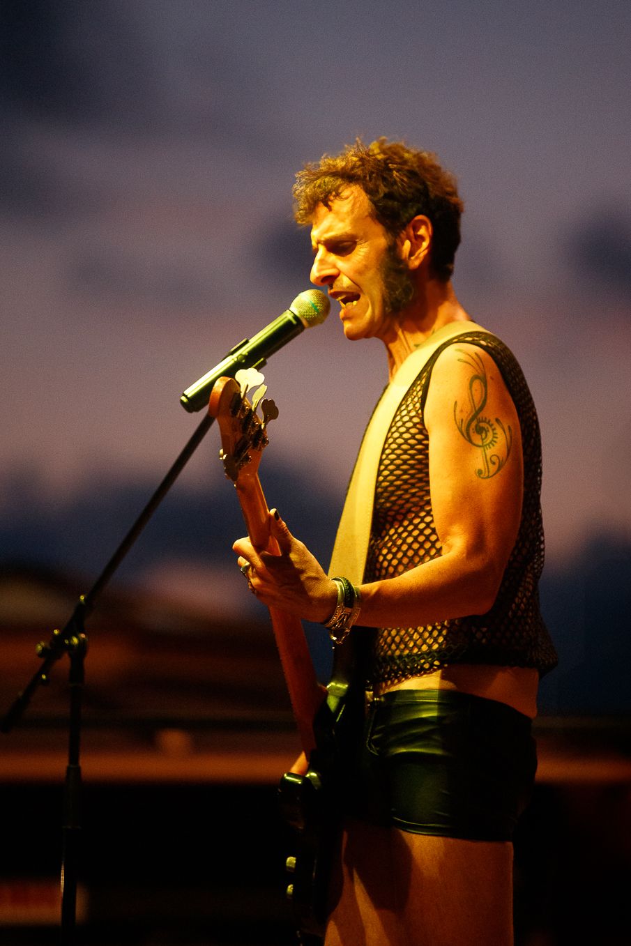 Performer with guitar singing into microphone under warm stage lighting.