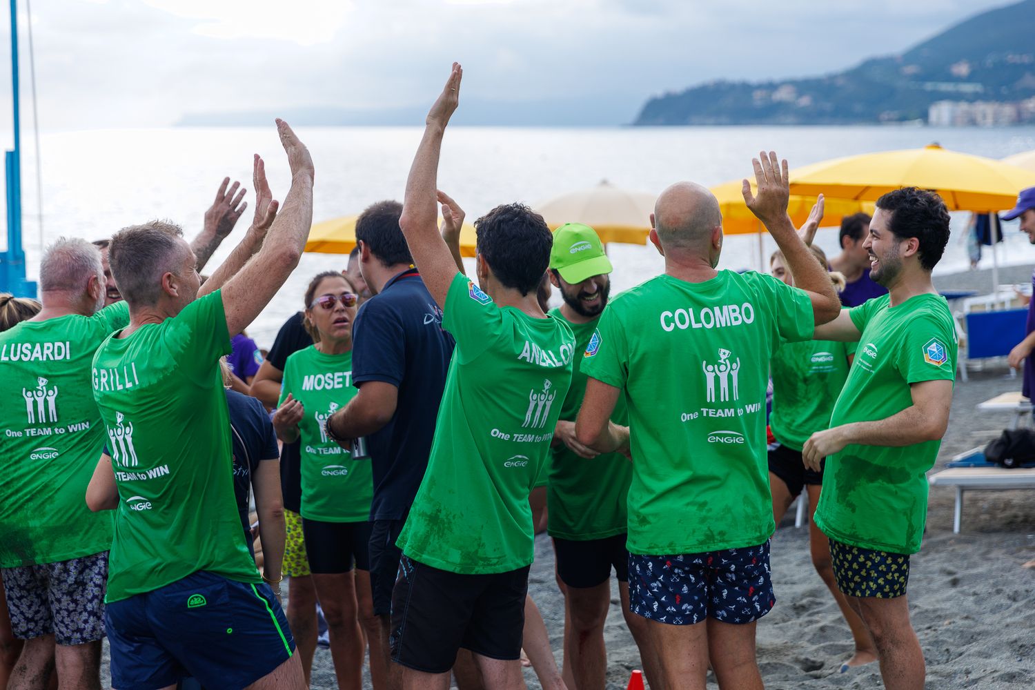 Group of people wearing matching green t-shirts celebrating together on a beach.