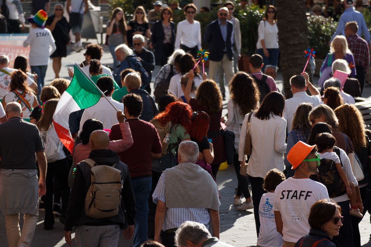 Crowd of people gathering outdoors with flags and protest signs.