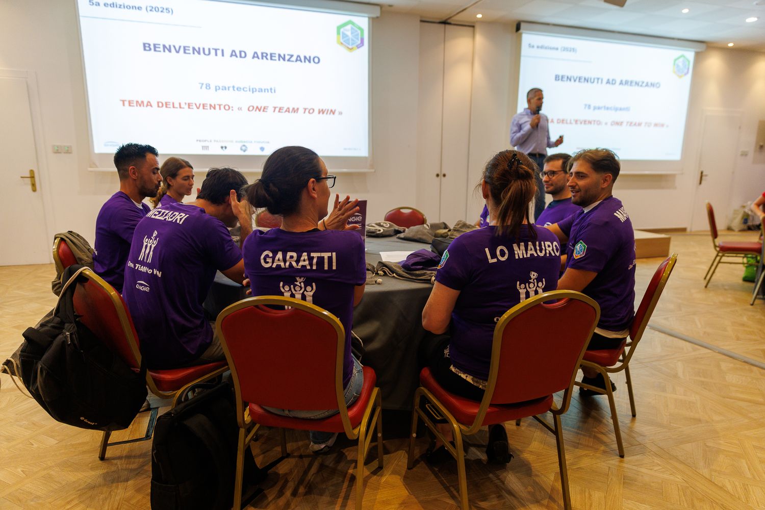 Conference attendees in purple shirts gathered for a training session in a meeting room.