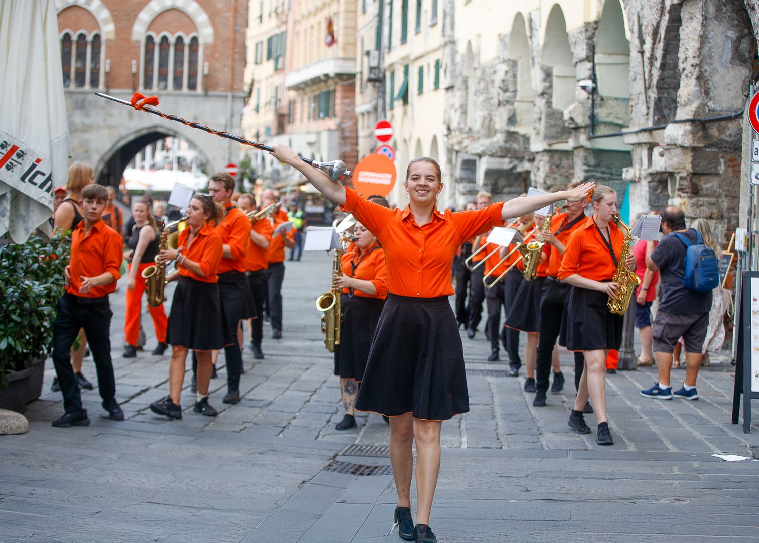 Street parade with performers in orange and black costumes walking through historic city streets.