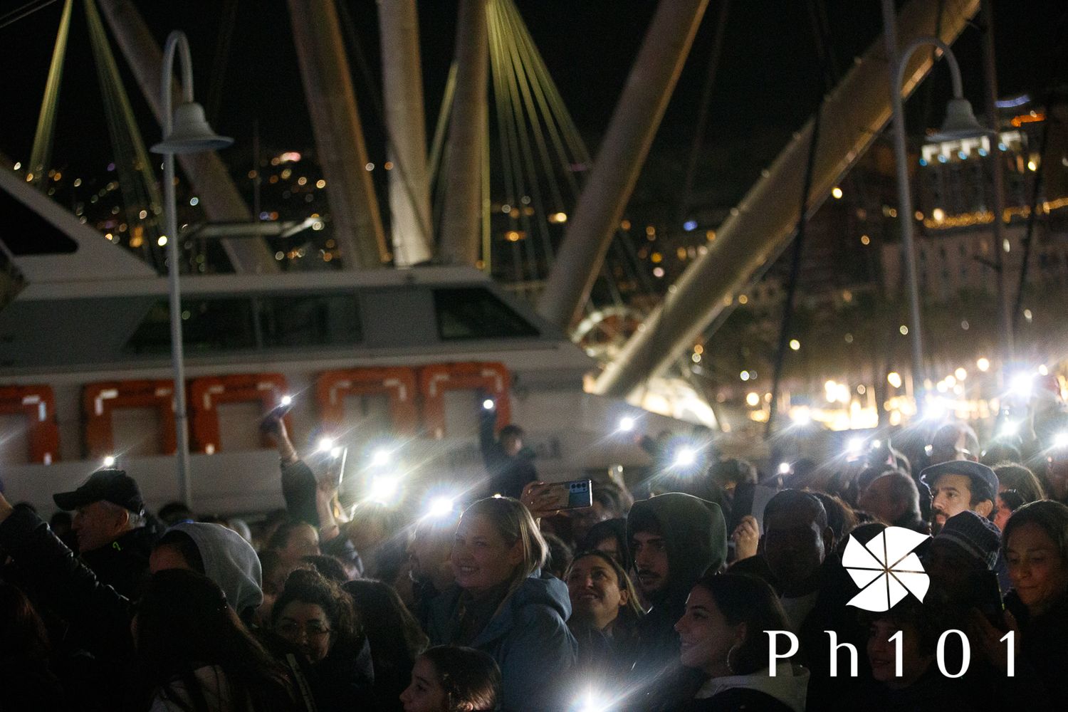 Concert crowd illuminated by bright lights and phone screens.