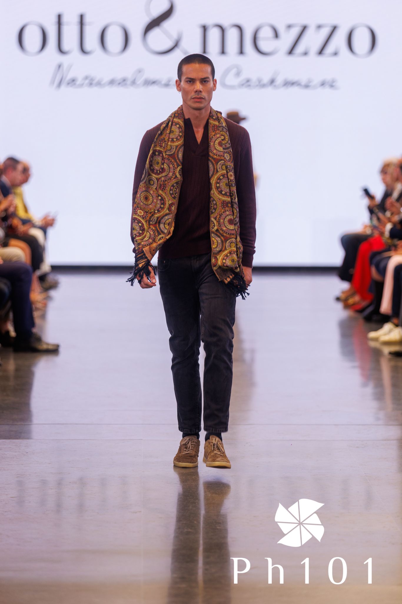 Fashion model presents black outfit with ornate gold-patterned vest on catwalk.