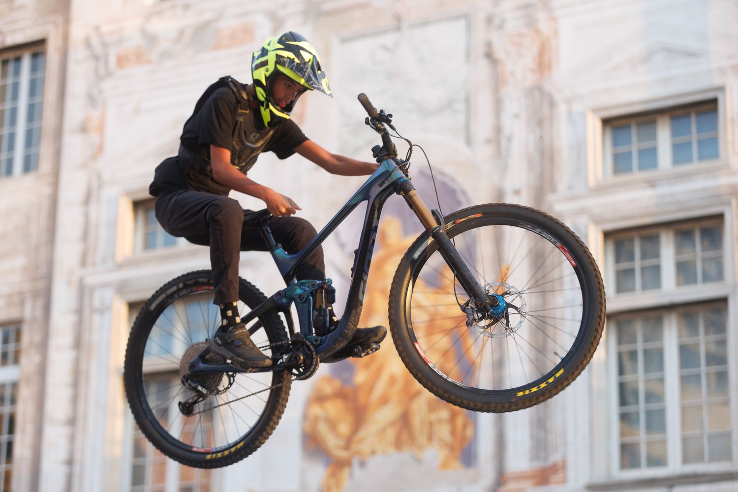 Multiple BMX riders perform synchronized aerial stunts in front of an ornate stone building.