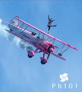 Pink and white stunt planes perform aerial maneuvers against a bright blue sky.