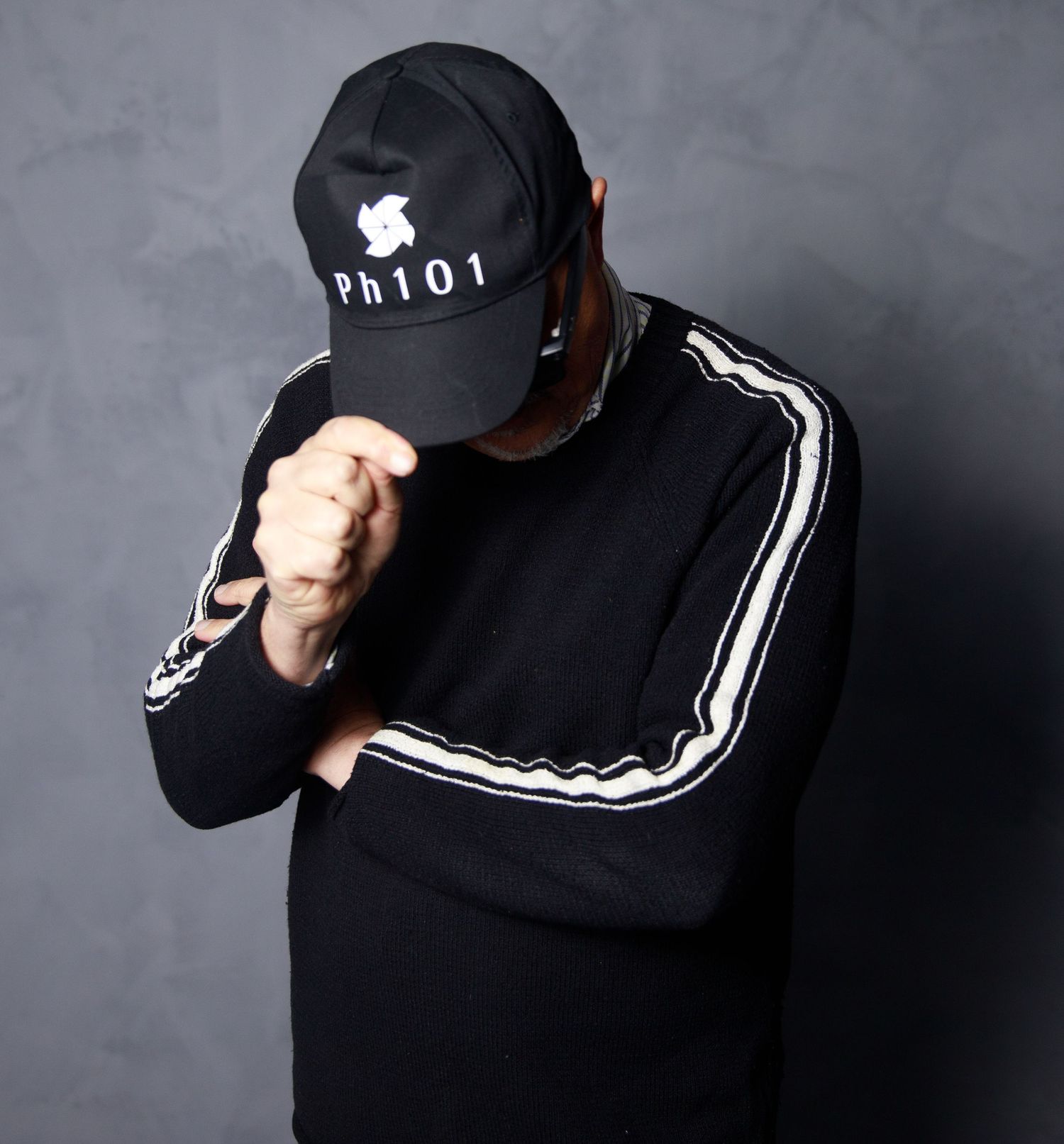 Person wearing black baseball cap and jacket with white stripes in dramatic studio lighting.