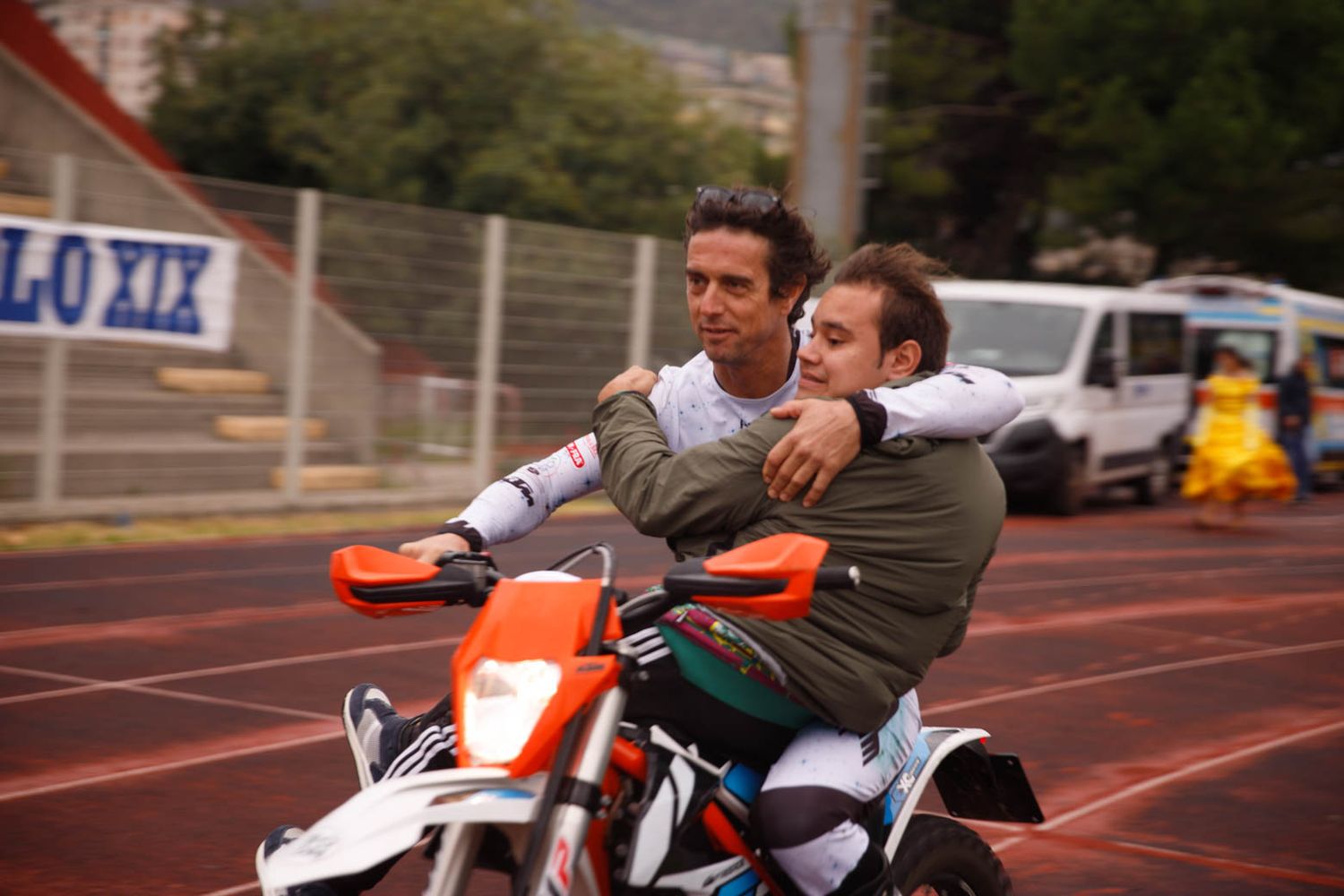 Athletes practicing on an outdoor track with motorcycles in the background.