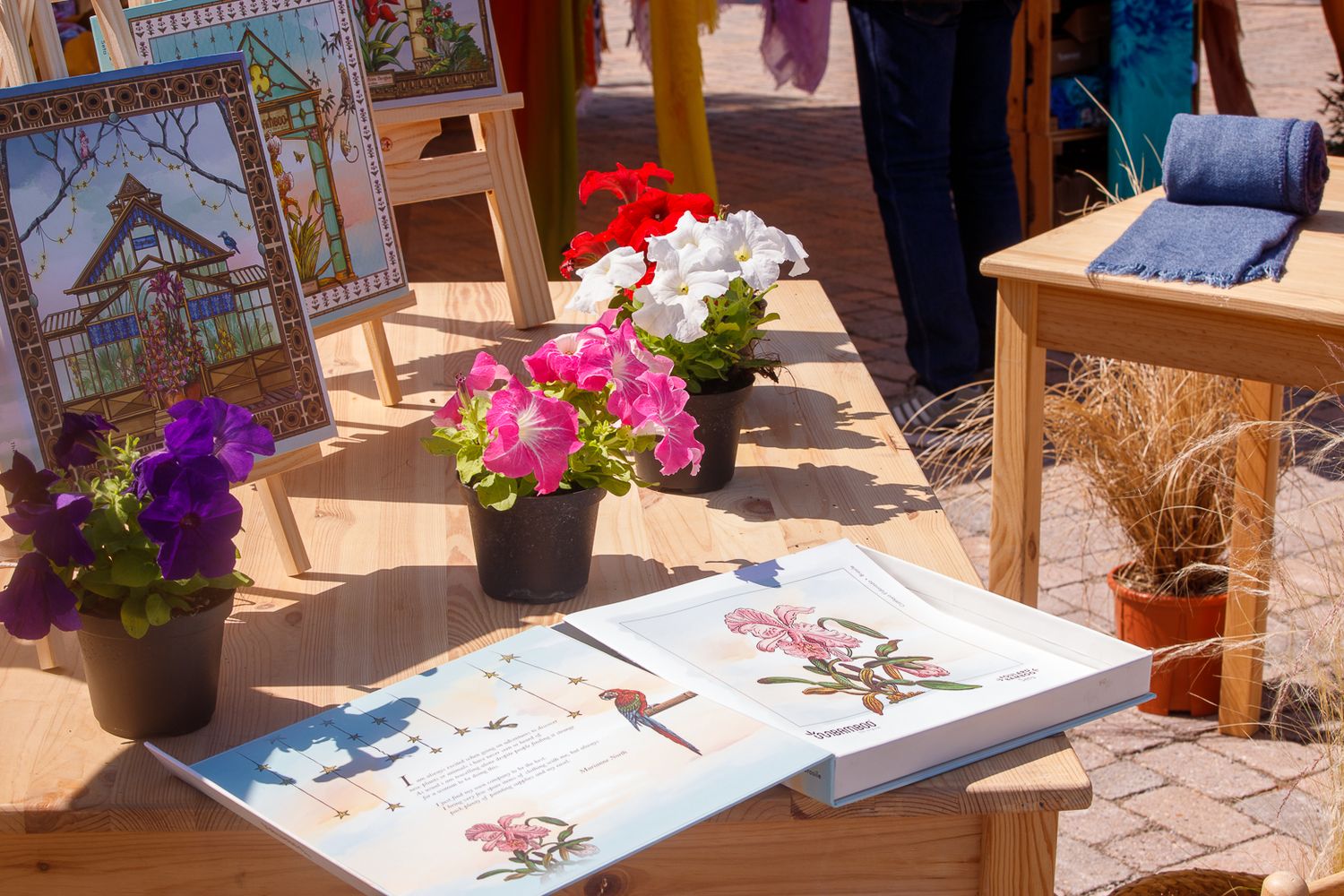 Outdoor market display with artwork and potted flowers on sunny day.
