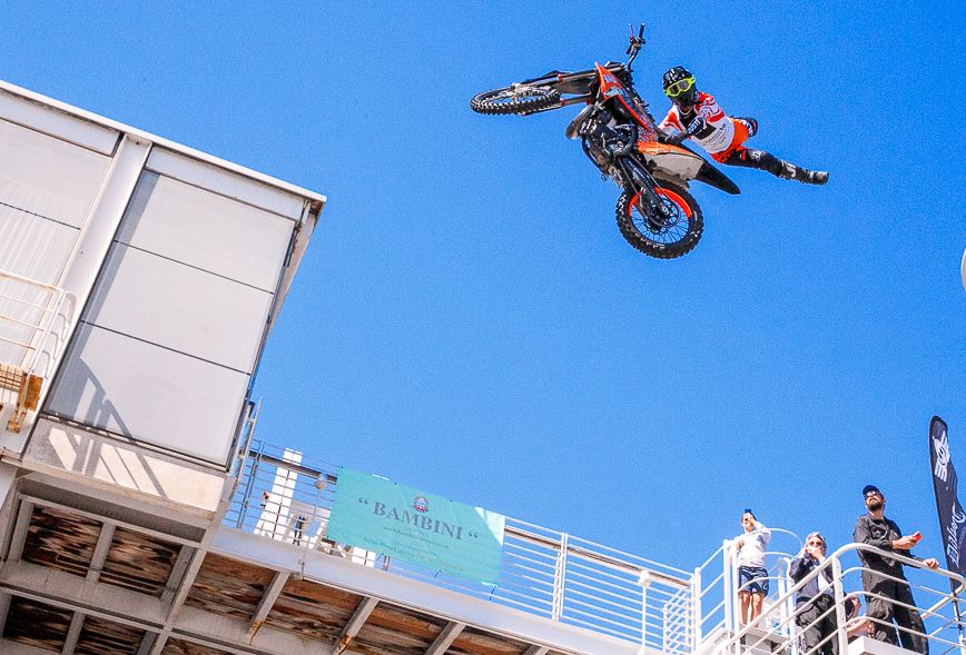Motocross rider performing aerial stunt jump against blue sky.