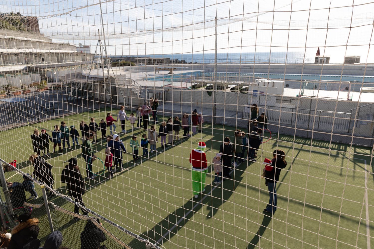 Soccer field enclosed by mesh netting with spectators gathered around the perimeter.