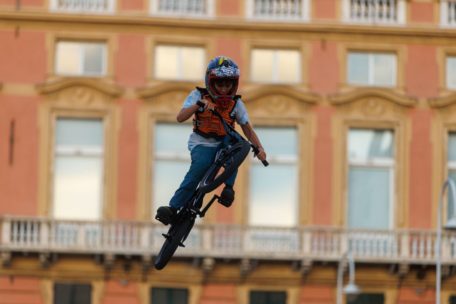 Person performing aerial stunt jump against orange building facade in urban setting.