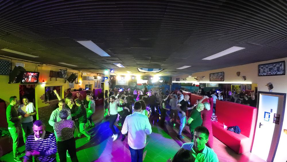 Crowded indoor event space with colorful disco lighting and dancing participants.