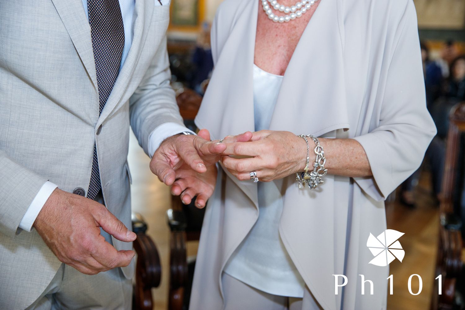 Close-up details of formal attire showing light gray suit jacket and pearl accessories.