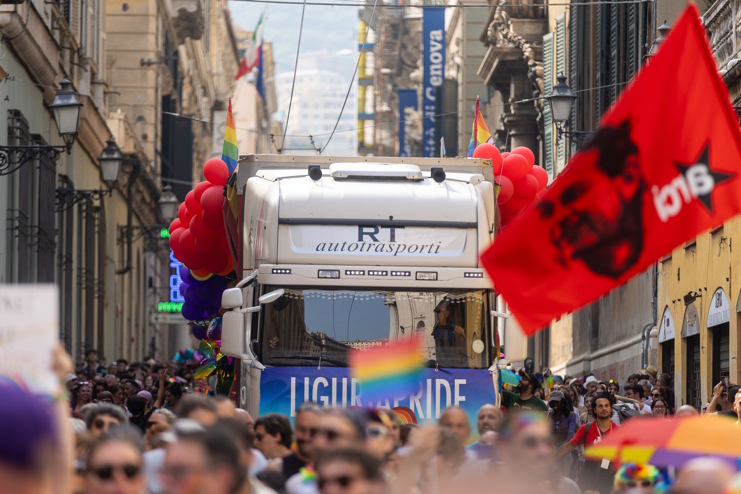 Urban street parade with red flags and marching participants.