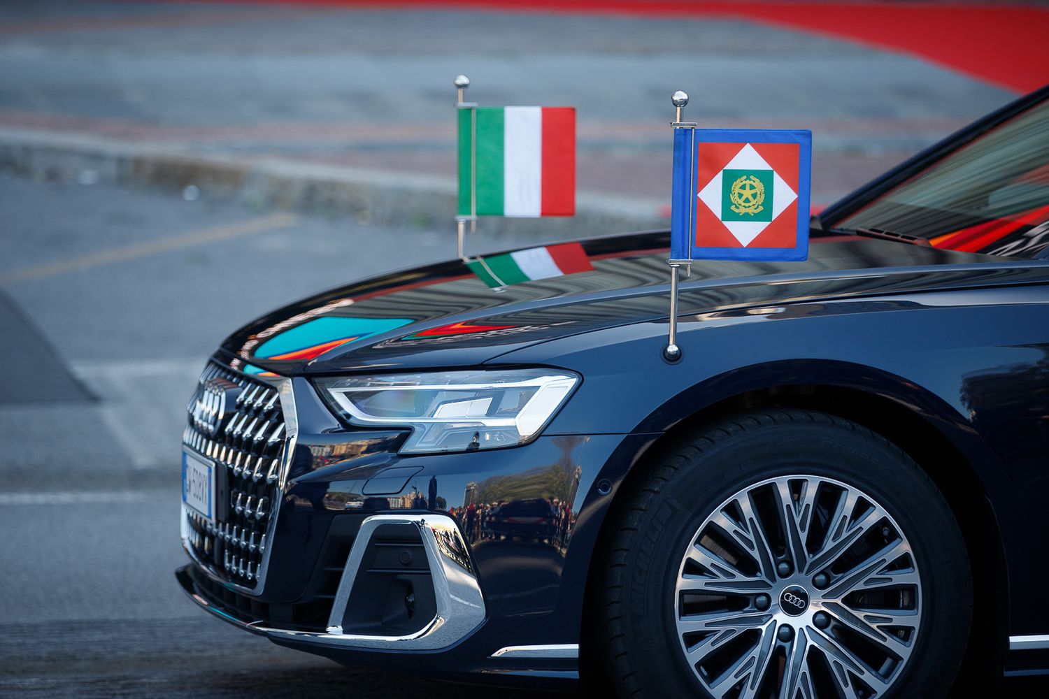 Luxury cars with Italian flags and military insignia displayed at formal event.