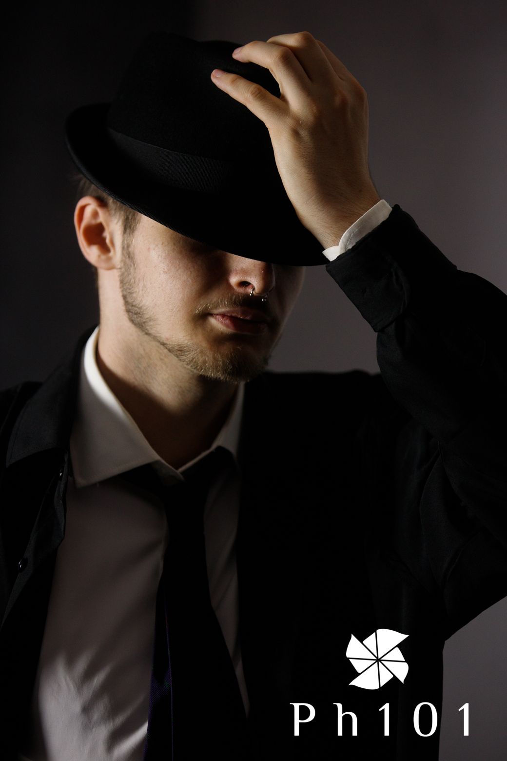 Dramatic lighting captures figure in formal wear adjusting fedora hat in shadow.